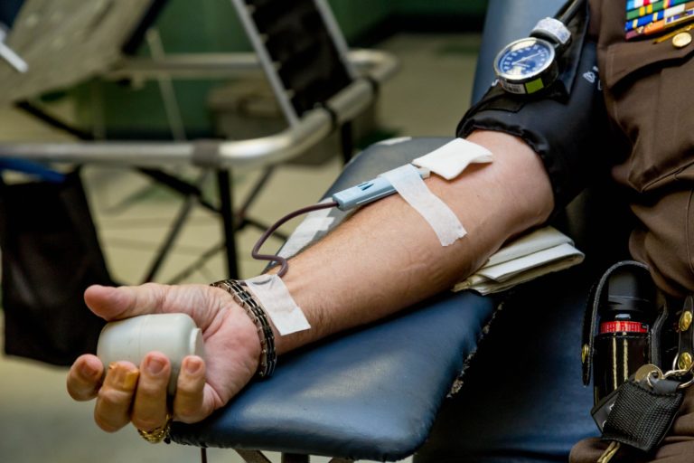 A imagem mostra um homem com o braço esticado doando sangue