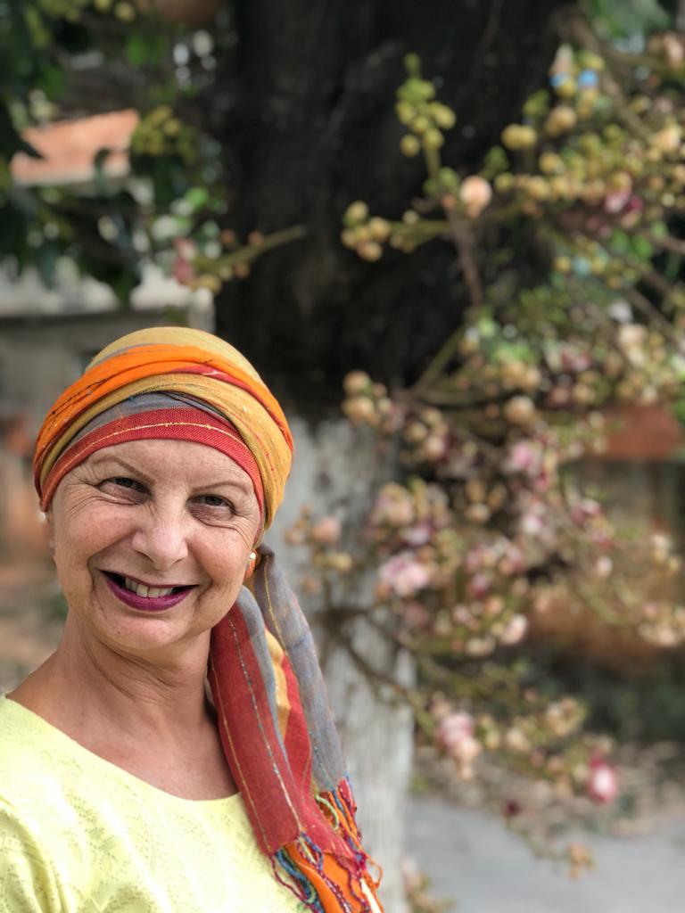 A imagem mostra Luzia, uma paciente com câncer usando um turbante em frente à uma árvore.