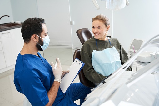 A imagem mostra um dentista conversando com sua paciente a respeito dos riscos do procedimento - o documento utilizado para registrar essas informações é o termo de consentimento livre e esclarecido